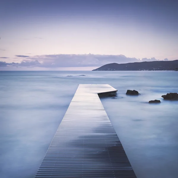 Träbrygga, klippor och havet på dimmig sunset. — Stockfoto