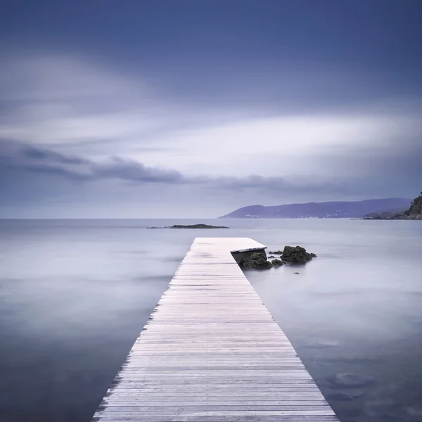 Wooden pier, rocks and sea on misty sunset. — Stock Photo, Image