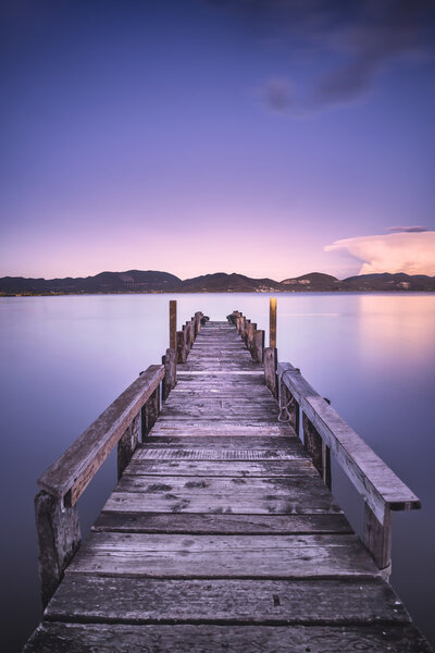 Wooden pier or jetty on a blue lake sunset and sky reflection on