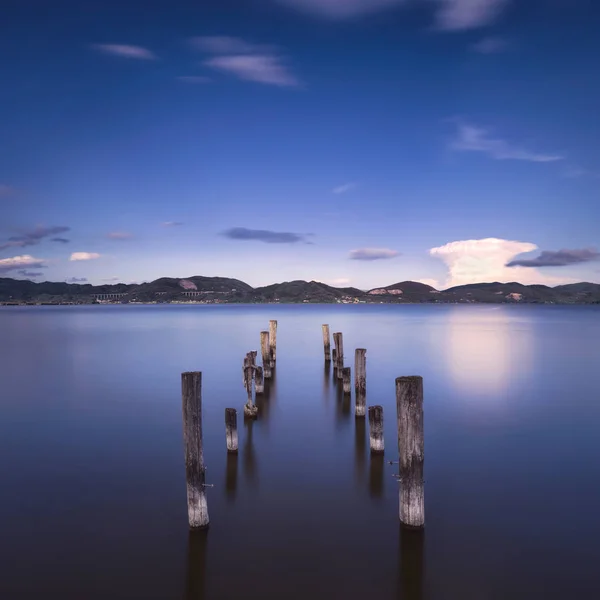 Wooden pier or jetty remains on a blue lake sunset and sky refle — Stock Photo, Image