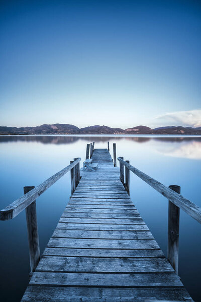 Wooden pier or jetty on a blue lake sunset and sky reflection on