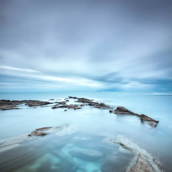 Dark rocks in a blue ocean under cloudy sky in a bad weather. Stock Image