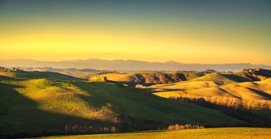 Volterra panorama, günbatımında inişli çıkışlı tepeler ve yeşil alanlar. Tus