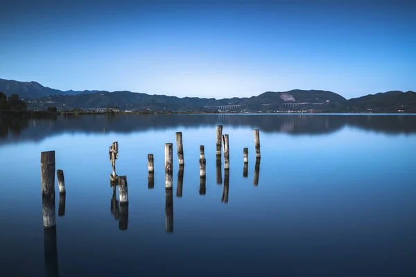 Wooden pier or jetty remains on a blue lake sunset and sky refle — Stock Photo, Image