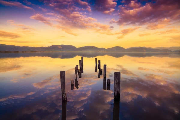 Muelle de madera o embarcadero permanece en un cálido atardecer lago y refle cielo — Foto de Stock