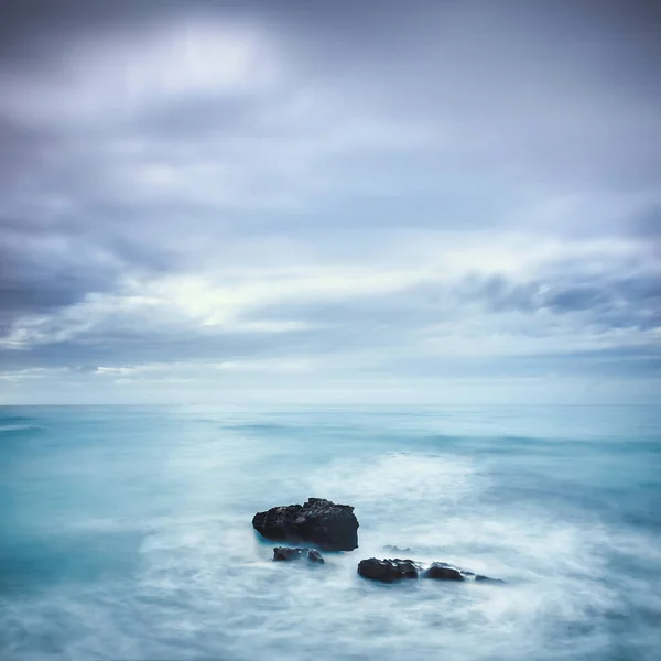 Rocas oscuras en un océano azul bajo el cielo nublado en un mal tiempo . — Foto de Stock