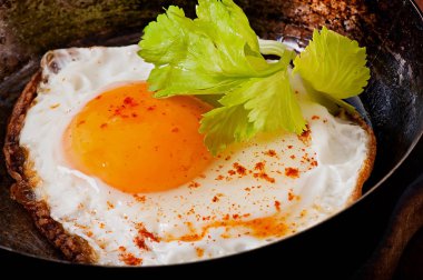 Bir tavada kızarmış yumurta ile acı biber serpilir.