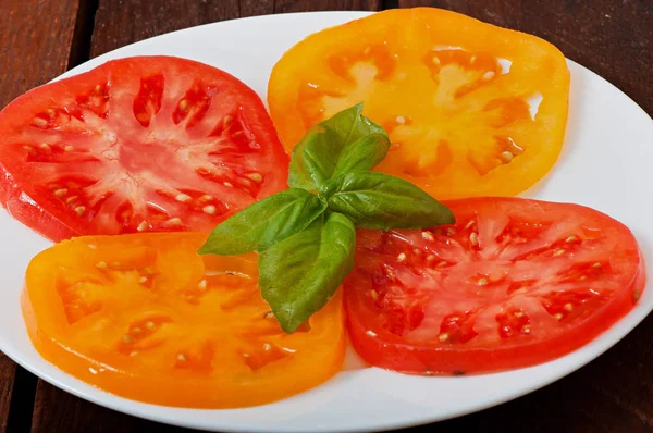 Červená a žlutá rajčata, plátky, na talíři. — Stock fotografie