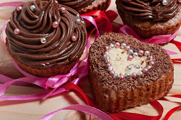 Chocolate cupcakes with chocolate cream and cupcake in the shape of heart, decorated with ribbon, on a wooden background. Valentine\'s Day.