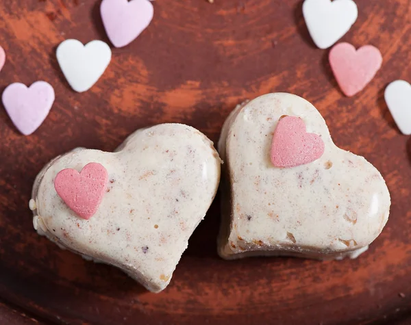 Milk sesame sweets in the form of heart, on a brown plate on an old wooden background.