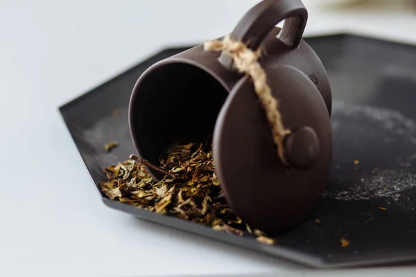 Beyaz bir masaya serpilmiş yeşil çayla kil bardak.