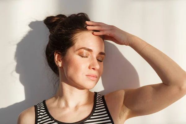 Genç ve çekici esmer kız beyaz bir duvarın yanında farklı duyguları, sert ışığı, ışığı ve gölgesi olan.