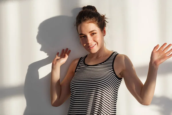 Genç ve çekici esmer kız beyaz bir duvarın yanında farklı duyguları, sert ışığı, ışığı ve gölgesi olan.