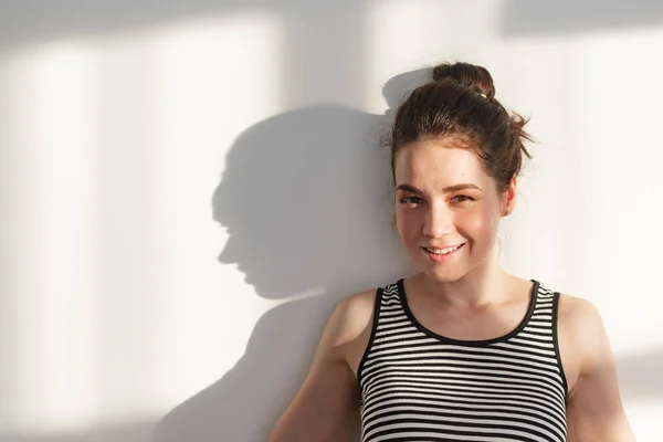 Genç ve çekici esmer kız beyaz bir duvarın yanında farklı duyguları, sert ışığı, ışığı ve gölgesi olan.