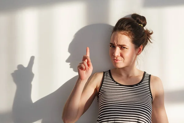 Genç ve çekici esmer kız beyaz bir duvarın yanında farklı duyguları, sert ışığı, ışığı ve gölgesi olan.