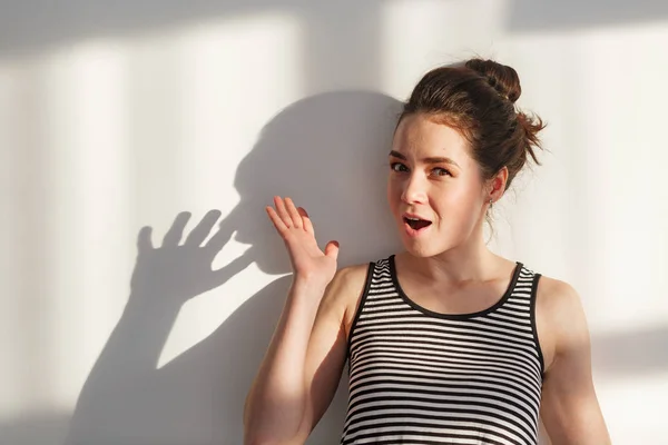 Genç ve çekici esmer kız beyaz bir duvarın yanında farklı duyguları, sert ışığı, ışığı ve gölgesi olan.