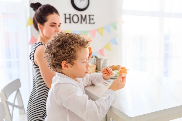 Genç, siyah saçlı mutlu annesi ve kıvırcık sarı oğlu Paskalya için İskandinav tarzında beyaz mutfakta yumurta boyuyorlar.