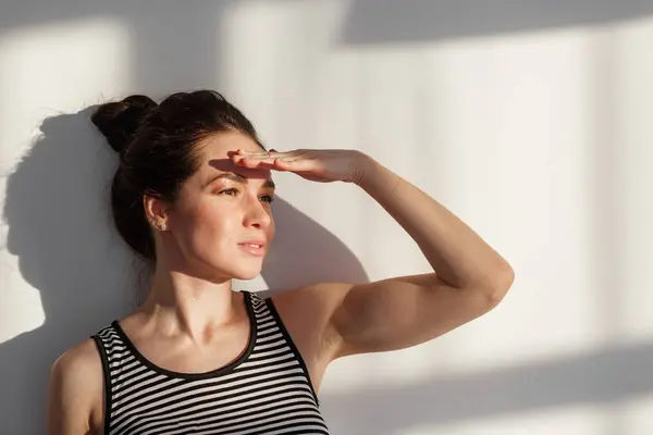 Genç ve çekici esmer kız beyaz bir duvarın yanında farklı duyguları, sert ışığı, ışığı ve gölgesi olan.