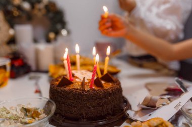 Çocuklar beyaz bir masada doğum günü pastasında mum yakıyor.