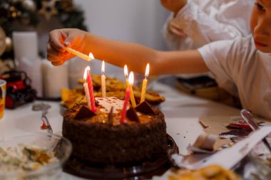Çocuklar beyaz bir masada doğum günü pastasında mum yakıyor.
