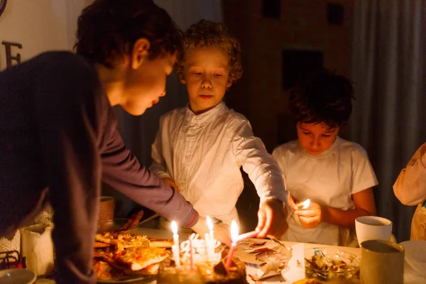 Çocuklar beyaz bir masada doğum günü pastasında mum yakıyor.