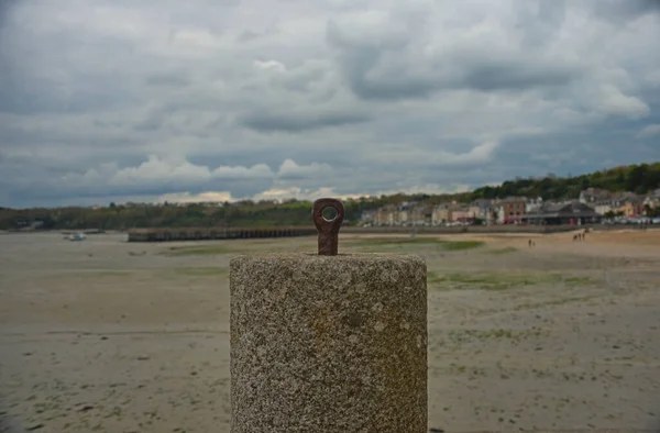 Concrete block for anchoring boats with sandy beach coastal town in background — Stock Photo, Image