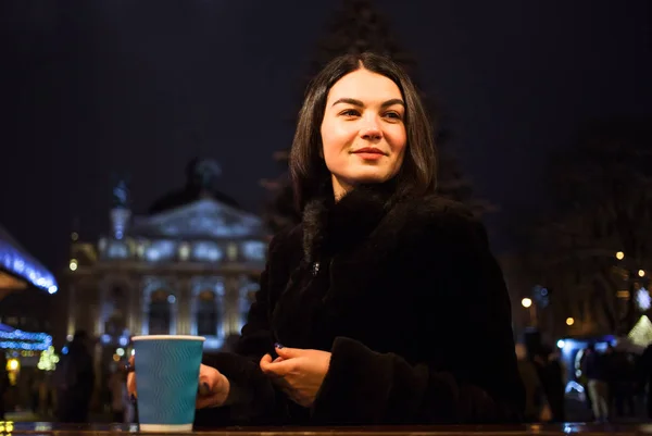 Красивая молодая девушка пьет горячий кофе на Рождественской ярмарке. Лига, город, зима, отпуск — стоковое фото