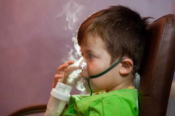 Little boy in a mask, treatments respiratory tract with a nebulizer at home. Baby sits with a nebulizer in his mouth, inhaler, treatment of bronchitis — Stock Photo, Image