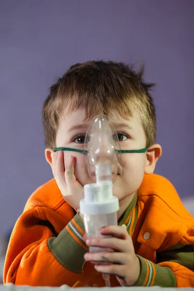 Menino em uma máscara, tratamentos trato respiratório com um nebulizador em casa. Bebê senta com um nebulizador em sua boca, inalador, tratamento de bronquite — Fotografia de Stock