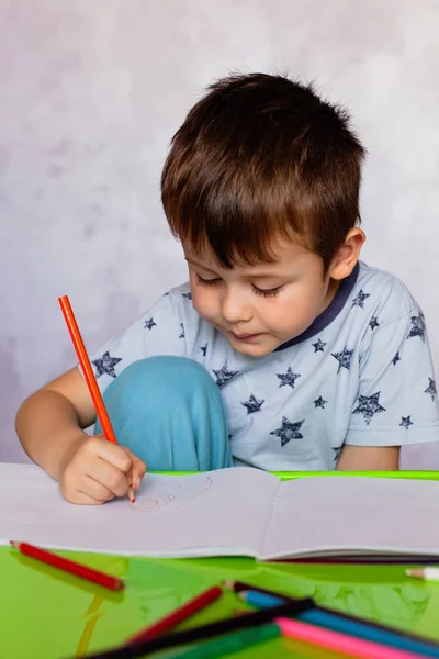 Kisfiú rajzol színes ceruzákkal. Fiú, apák napjára rajzolsz egy képet. Kisfiú rajzol az asztalnál.. — Stock Fotó