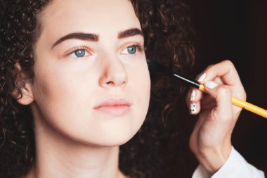 Profesyonel bir makyözün işi. Güzel bir kadının yakın plan portresi fırçayla profesyonel makyaj yaptırıyor..