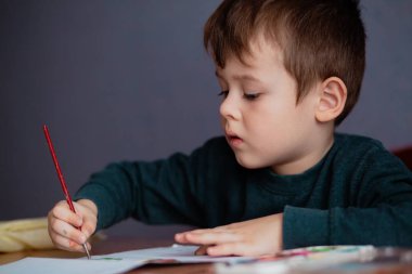 Küçük çocuk bir fırça çeker ve ilk resmini çizer. Küçük şirin bir çocuğun resim çizdiği yakın plan portresi..