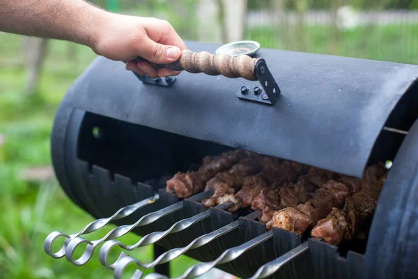 男の手が金属製の火鉢を開ける 金属串を閉じる上で焼きケバブ料理 自然の中で夏のピクニック — ストック写真