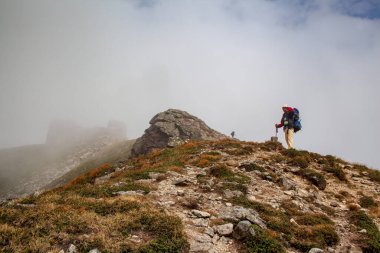 Sırt çantalı yürüyüşçü yokuş yukarı gidiyor. Karpat dağlarında yürüyüş. Yürüyüşçü çok dik bir patikada dağın zirvesine çıkıyor. Yaşam tarzı konsepti aktif turizm