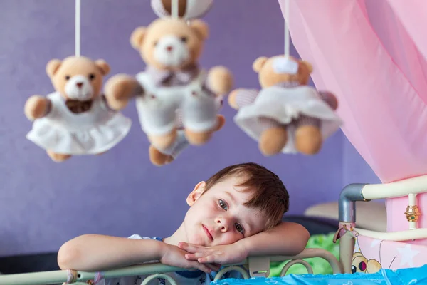 Adorable little boy standing near cot with Baby music mobile carousel. Big Brother watches younger sister in crib. Toy carousel, above the baby bed.