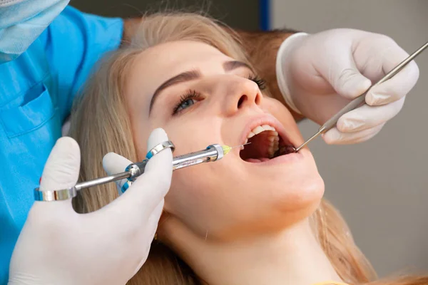 The dentist showing teeth x-ray to the patient on tablet, explaining the problem using smart technology. Pretty woman smiles sitting in dental chair