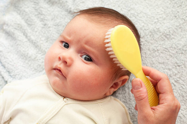 Hand brushing a baby's hair with a soft brush. Maternity concept. Baby hygiene