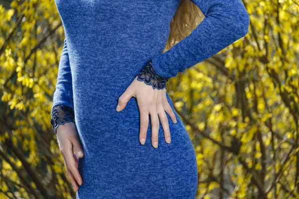 Mão na cintura de uma menina esbelta em um vestido azul contra um fundo amarelo — Fotografia de Stock