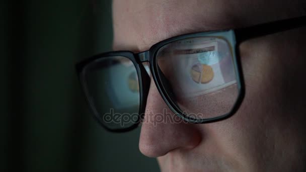 一个办公室工作人员坐在电脑旁 一台表和图表的显示器被反映在眼镜里 — 图库视频影像