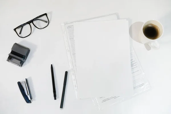 paper, pens, stapler and glasses on a white background. office white table.