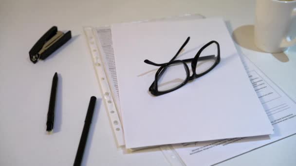 那人从桌子上拿起他的眼镜 白色背景的纸和笔 — 图库视频影像
