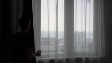 genç adam şehir pencereden dışarı bakar ve çay içer