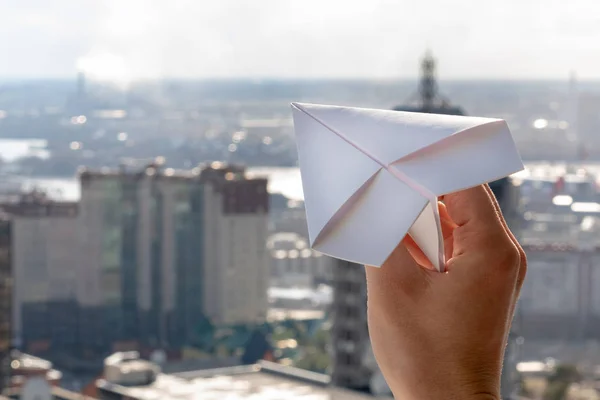 man\'s hand launches a paper airplane in a window against the background of city and sky