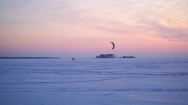 Donmuş gölün üzerinde güzel bir gün batımı ve karda kayak yapan uçurtmacılar..