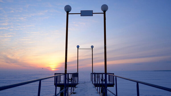 A frozen pier against the backdrop of an icy snow-covered field and a beautiful sunset.
