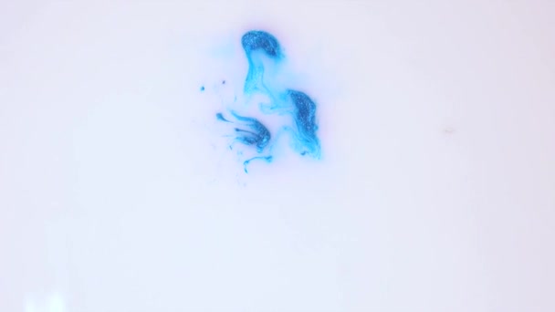 輝きのある青色の塗料の滴は白い液体に落ち 美しいパターンのクローズアップで溶解します — ストック動画