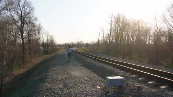 Kız tek başına demiryolu rayları boyunca gider güneşli gökyüzünün arka planına karşı.