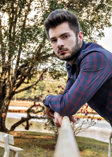 Rapaz debruado sobre ponte com olhar indagativo