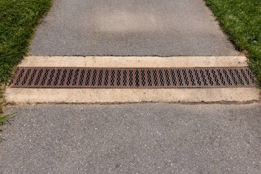 Yaz günü yeşil çimenli yaya geçidinde, kanalizasyon sisteminin ızgara kapaklı demir oluğu..