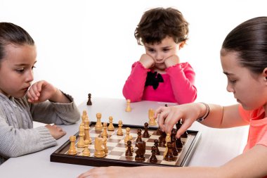 Kız kardeşler birlikte satranç oynuyorlar. Beyazlar üzerinde izole edilmiş. Çocuk konsantrasyonu kavramı.